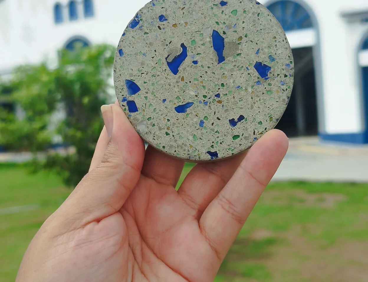 Mão segurando uma peça circular de concreto com areia de vidro reciclado