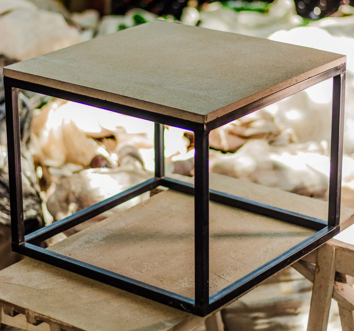 Mesa de centro quadrada com tampo de concreto e areia de vidro sobre estrutura de metal preta